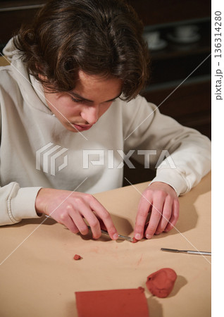 Focused Boy Molding Clay at Home, Engaged in Creative Hobby Project 136314280