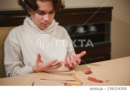 Young Boy Crafting Clay At Home: Focused Hobbyist With Tools And Red Clay Pieces Young Boy Crafting Clay At Home: Focused Hobbyist With Tools And Red Clay Pieces 136314300