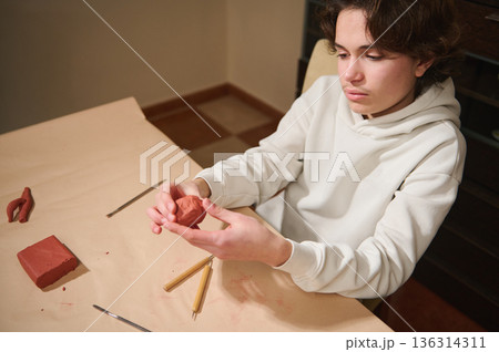 Teen Boy Sculpting Red Clay At Home: Craft Hobby In Workshop Teen Boy Sculpting Red Clay At Home: Craft Hobby In Workshop 136314311