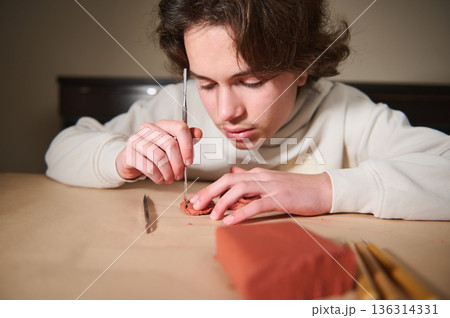 Young Boy Focused On Clay Molding With Tools At Home, Concentration And Creativity 136314331