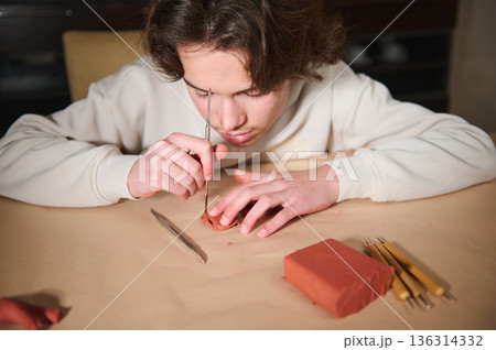 Young Boy Molding Clay at Home, Focused on Sculpting with Tools and Red Clay Block 136314332