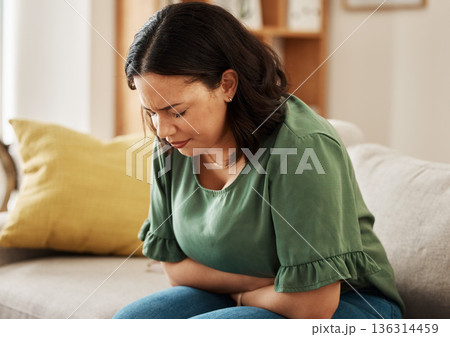 Stomach pain, stress and woman on a sofa with pms, gas or bloating, constipation or menstrual nausea at home. Gut health, anxiety and female in living room with tummy ache, anxiety or endometriosis 136314459