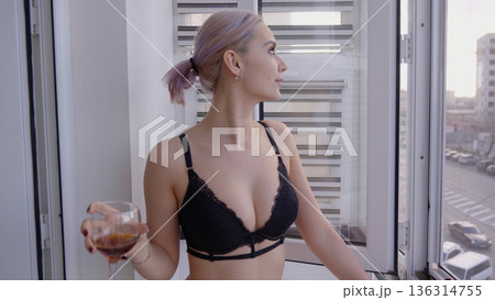 Young woman standing near window with glass of wine Young woman standing near window with glass of wine 136314755