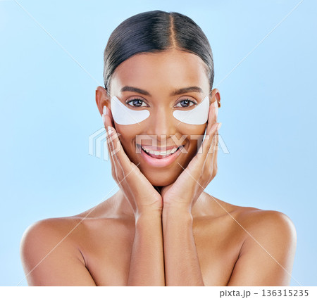 Beauty, skincare and portrait of woman with patches for eyes, dark circles and treatment. Smile, spa and Indian girl or model with a facial product for a glow isolated on a blue background in studio 136315235