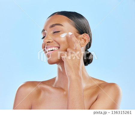 Face cream, skin and beauty of a happy woman with natural glow on a blue background. Dermatology, moisturizer and cosmetics of an Indian female model for facial shine, wellness or self care in studio 136315261