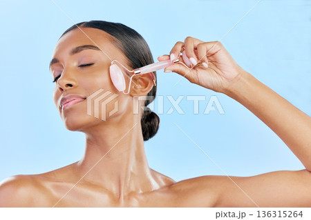 Facial massage, woman and roller, natural beauty and skincare, cosmetics and tools isolated on blue background. Rose quartz, crystal and skin glow, Indian female model with dermatology and antiaging Facial massage, woman and roller, natural beauty and skincare, cosmetics and tools isolated on blue background. Rose quartz, crystal and skin glow, Indian female model with dermatology and antiaging 136315264