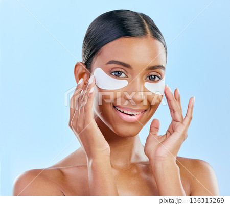 Happy, skincare and portrait of woman with patches for eyes, dark circles and treatment. Smile, face and Indian girl or model with a facial collagen for a glow isolated on a blue background in studio Happy, skincare and portrait of woman with patches for eyes, dark circles and treatment. Smile, face and Indian girl or model with a facial collagen for a glow isolated on a blue background in studio 136315269