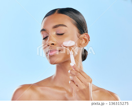 Facial massage, woman and roller, beauty and skincare, natural cosmetics and tools isolated on blue background. Rose quartz, crystal and skin glow, Indian female model with dermatology and antiaging Facial massage, woman and roller, beauty and skincare, natural cosmetics and tools isolated on blue background. Rose quartz, crystal and skin glow, Indian female model with dermatology and antiaging 136315275