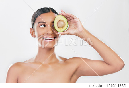 Avocado, eye skincare and happy woman isolated on a white background for healthy facial and cosmetics ideas. Indian person or beauty model thinking of green, vegan or dermatology product in studio Avocado, eye skincare and happy woman isolated on a white background for healthy facial and cosmetics ideas. Indian person or beauty model thinking of green, vegan or dermatology product in studio 136315285