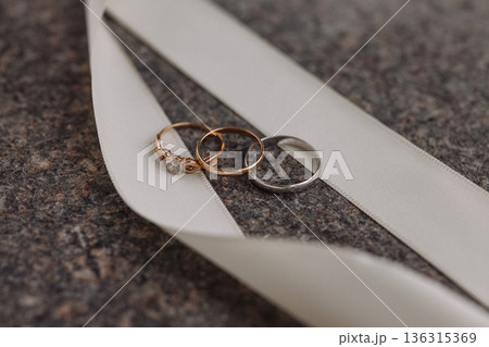 Wedding rings on white ribbon on dark stone surface Wedding rings on white ribbon on dark stone surface 136315369