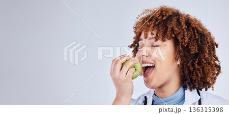 Doctor, woman and eating apple in studio, white background and mockup space. Face of medical employee, happy female nutritionist and bite fruits for vitamin c nutrition, healthy food and vegan diet 136315398