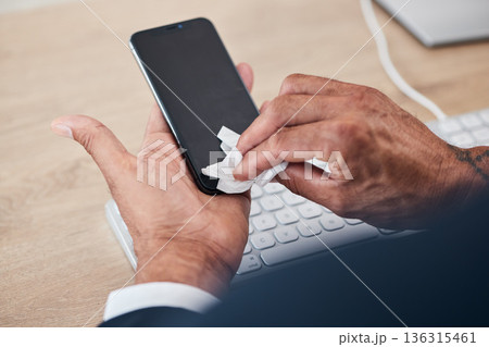 Closeup of man wipe his phone with a tissue to prevent germs, bacteria or dirt in his office. Technology, hands and male person cleaning cellphone screen for hygiene, health and wellness at workplace 136315461