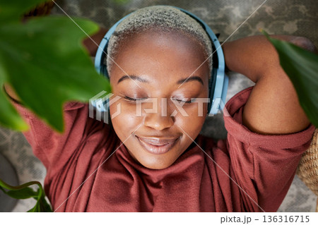 Woman, face and headphones for listening to music to relax on a floor with plants for peace and calm. Headshot of a black female person meditate with sound, audio and podcast or radio at home 136316715
