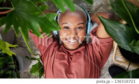 Headphones, portrait and woman listening to music to relax with plants for peace and calm. Face of a happy black female person streaming sound, audio and podcast or radio online with a smile at home Headphones, portrait and woman listening to music to relax with plants for peace and calm. Face of a happy black female person streaming sound, audio and podcast or radio online with a smile at home 136316721