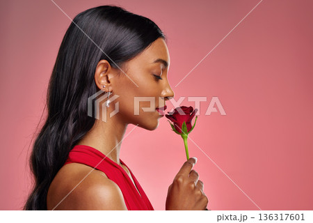 Face, woman and smelling a rose on a studio background for valentines day. Fragrance, model and profile of a young Indian girl with a flower in hand for romance, scent or love on pink backdrop 136317601