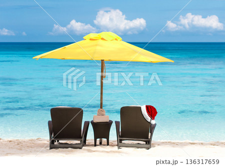 Santa Claus hat on sunbed on tropical beach with sun umbrellas and chaise longues. Christmas and New Year celebration Santa Claus hat on sunbed on tropical beach with sun umbrellas and chaise longues. Christmas and New Year celebration 136317659