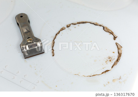 Special steel scraper on dirty white ceramic kitchen stove after cooking. Concept of homecleaning Special steel scraper on dirty white ceramic kitchen stove after cooking. Concept of homecleaning 136317670