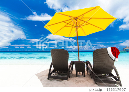 Santa Claus hat on sunbed on tropical beach with sun umbrellas and chaise longues. Christmas and New Year celebration 136317697