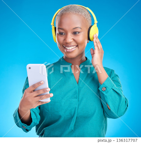 Headphones, phone and woman listening on studio, blue background for podcast, music and streaming service. Mobile, audio technology and young african woman on electronics for radio, sound or hearing Headphones, phone and woman listening on studio, blue background for podcast, music and streaming service. Mobile, audio technology and young african woman on electronics for radio, sound or hearing 136317707