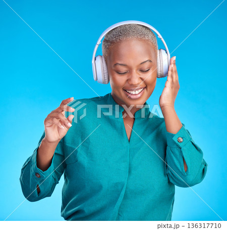 African woman, headphones and studio for listening, music and smile with dancing by blue background. Young gen z student, sound tech and happy for audio streaming, online radio and excited with dance African woman, headphones and studio for listening, music and smile with dancing by blue background. Young gen z student, sound tech and happy for audio streaming, online radio and excited with dance 136317710