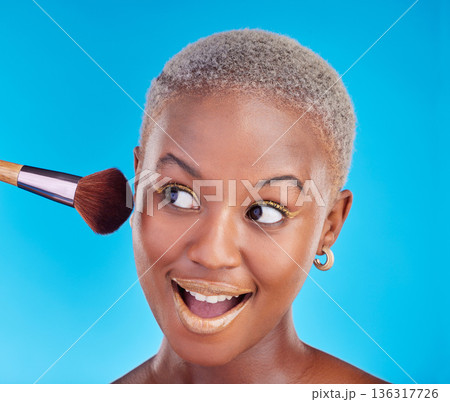 Black woman, face and brush of makeup in studio for application of foundation on blue background. Happy female model, wow and brushing beauty powder on skin with cosmetic tools for facial aesthetic Black woman, face and brush of makeup in studio for application of foundation on blue background. Happy female model, wow and brushing beauty powder on skin with cosmetic tools for facial aesthetic 136317726