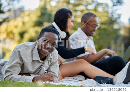 Nature, university and portrait of a man studying on the grass with his friends for a test or exam. Happy, smile and African male student writing assignment in his notebook in park at college campus. 136318051