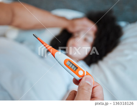 Thermometer, temperature and parent with a sick child, fever and health check in a home bedroom. Medical, care and hand of a man with a tool for covid results, virus and a cold of a girl in a bed 136318126
