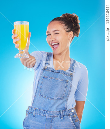 Happy woman, portrait and juice for vitamin C, diet or healthy drink against a blue studio background. Female person or model with denim fashion holding glass with organic fruit blend or breakfast Happy woman, portrait and juice for vitamin C, diet or healthy drink against a blue studio background. Female person or model with denim fashion holding glass with organic fruit blend or breakfast 136318434
