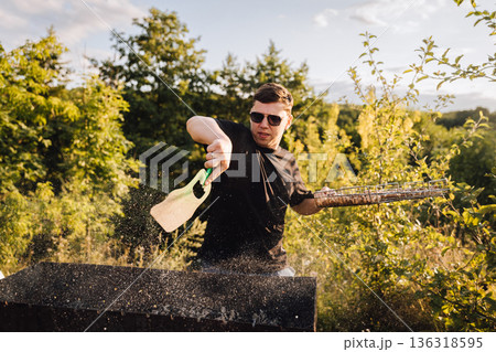 Man fanning charcoal grill outdoors at sunset, sparks flying during summer barbecue Man fanning charcoal grill outdoors at sunset, sparks flying during summer barbecue 136318595