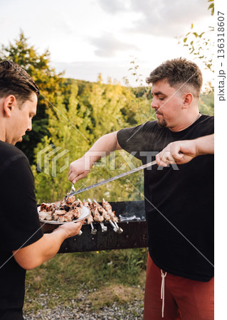 Man serving grilled pork shashlik from skewer to plate at outdoor barbecue Man serving grilled pork shashlik from skewer to plate at outdoor barbecue 136318607