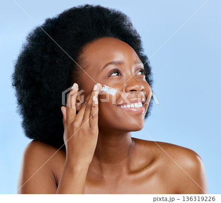 Black woman, face and cream, beauty and skincare with cosmetics on blue background. Moisturizer, lotion and product for skin with sunscreen and happiness, female model and dermatology in studio 136319226