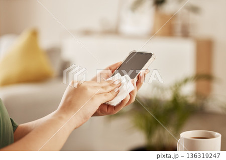 Closeup of a woman cleaning her phone with paper to prevent germs, dirt or dust bacteria at home. Hygiene, technology and female person wipe her cellphone to sanitize her screen in the living room. 136319247