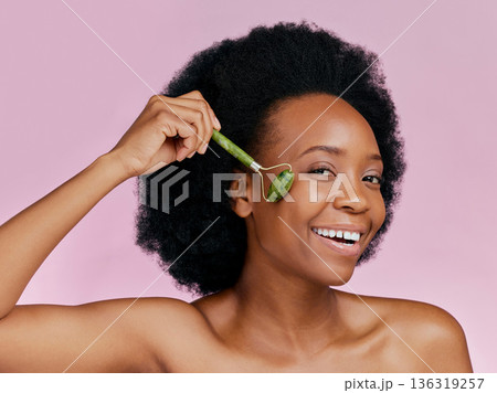 Happy, skincare and portrait of black woman with a jade roller for a facial massage or treatment. Smile, relax and African girl or model with a facial product isolated on a pink background in studio Happy, skincare and portrait of black woman with a jade roller for a facial massage or treatment. Smile, relax and African girl or model with a facial product isolated on a pink background in studio 136319257