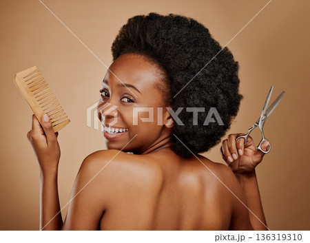 Portrait, back and a black woman with a comb and scissors in studio on a brown background for a haircut. Smile, afro and haircare with a happy young female person looking excited at the salon 136319310