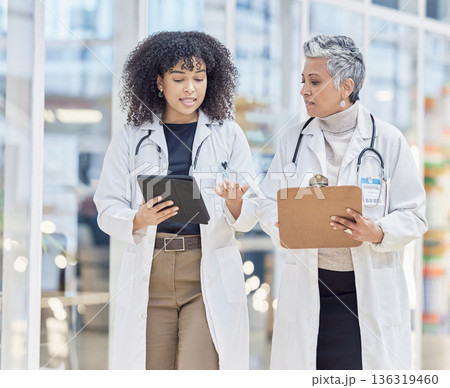 Team, tablet and documents with woman doctors walking in a hospital for insurance or healthcare discussion. Collaboration, trust and consulting with female medicine professionals talking in a clinic 136319460