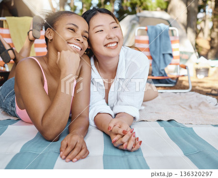 Happy, relax and girl friends on a picnic while on camp weekend trip in the woods or nature. Happiness, smile and young interracial female people resting on blanket in outdoor park, garden or forest. 136320297