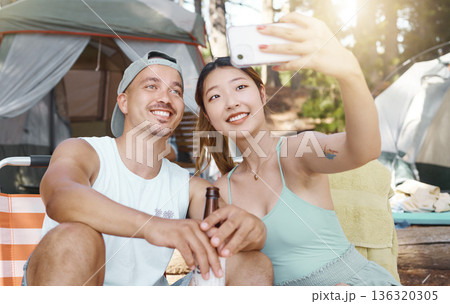 Selfie, love and young couple on a camp in the woods for a summer weekend trip or holiday. Happy, smile and man with beer while his girlfriend taking a picture in forest on outdoor vacation together. 136320305