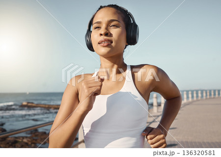 Fitness, woman run at beach and with headphones listening to music for training. Exercise or marathon, lens flare or sportswear and female athlete running along the promenade listen to radio Fitness, woman run at beach and with headphones listening to music for training. Exercise or marathon, lens flare or sportswear and female athlete running along the promenade listen to radio 136320581