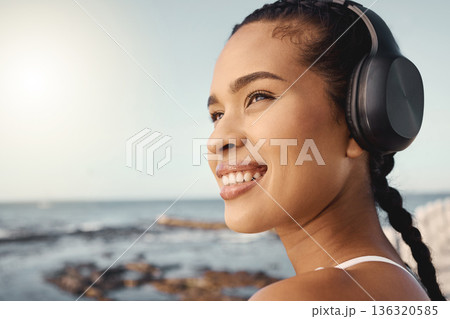 Headphones, fitness and happy woman at beach for exercise, vision or running mindset, goals or music ideas. Health, podcast and athlete, runner or sports person thinking and listening to audio by sea 136320585