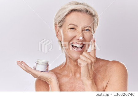 Portrait, cream and beauty with senior woman, happy with skincare and dermatology on white background. Sunscreen, moisturizer and face care, female model apply lotion with glass container and skin 136320740