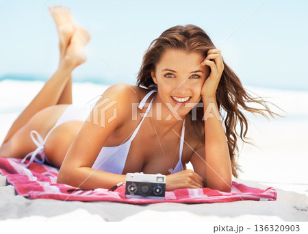 Happy woman, portrait and bikini in relax on beach for summer day, vacation or holiday in the outdoors. Female person in swimwear lying on towel by the ocean coast for weekend break or getaway by sea 136320903