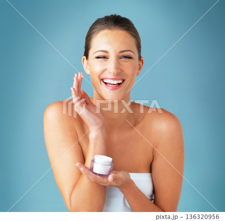 Skincare, dermatology and portrait of happy woman with cream, cosmetics and product on blue background. Lotion, skin care and wellness, model with smile, beauty treatment and facial glow in studio. 136320956