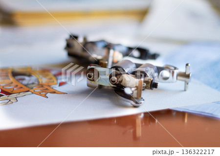 Creative, closeup and a tattoo gun for art, piercing or professional ink work in a studio. Creativity, tool and a machine or product for tattoos, artistic expression and needle for color on a desk Creative, closeup and a tattoo gun for art, piercing or professional ink work in a studio. Creativity, tool and a machine or product for tattoos, artistic expression and needle for color on a desk 136322217