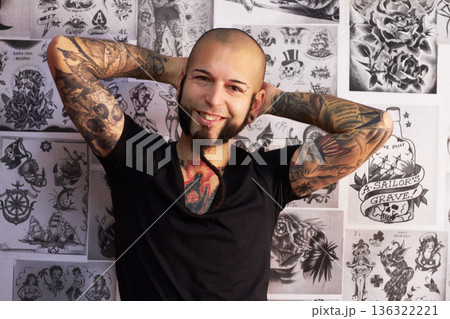 Tattoos, creativity and portrait of a male artist standing by sketches or drawings in his studio. Happy, smile and face of a punk man with a edgy, funky and body art or ink creative business store. 136322221