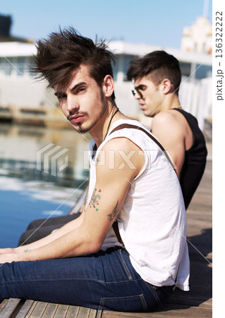 Portrait, gen z and friends sitting on a pier in a harbor together during summer vacation or holiday. Fashion, tattoo and trendy with an edgy young male person and his friend by the sea in a dock Portrait, gen z and friends sitting on a pier in a harbor together during summer vacation or holiday. Fashion, tattoo and trendy with an edgy young male person and his friend by the sea in a dock 136322222