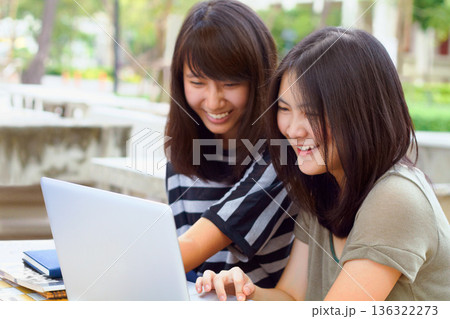 Laptop, university and female students studying outdoor on campus for a test, exam or assignment. Happy, smile and women doing research or browsing for education information on a computer at college. 136322273
