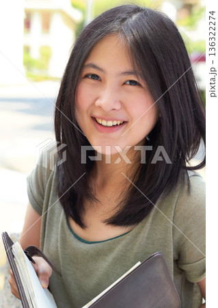 Portrait, education and book with an asian woman student on university campus for learning or development. Study, smile or happy with a young female college pupil outdoor to study or learn in summer 136322274