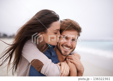 Woman kiss man, happiness and beach with holiday, travel and love with care and trust outdoor. Freedom, affection and fun with couple in nature, vacation and smile with support and hug by the ocean Woman kiss man, happiness and beach with holiday, travel and love with care and trust outdoor. Freedom, affection and fun with couple in nature, vacation and smile with support and hug by the ocean 136322361