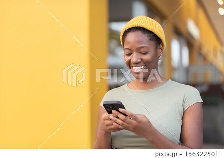 Smiling young black woman using smartphone against 136322501
