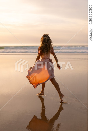 Woman in flowing dress walking barefoot on beach Woman in flowing dress walking barefoot on beach 136322509